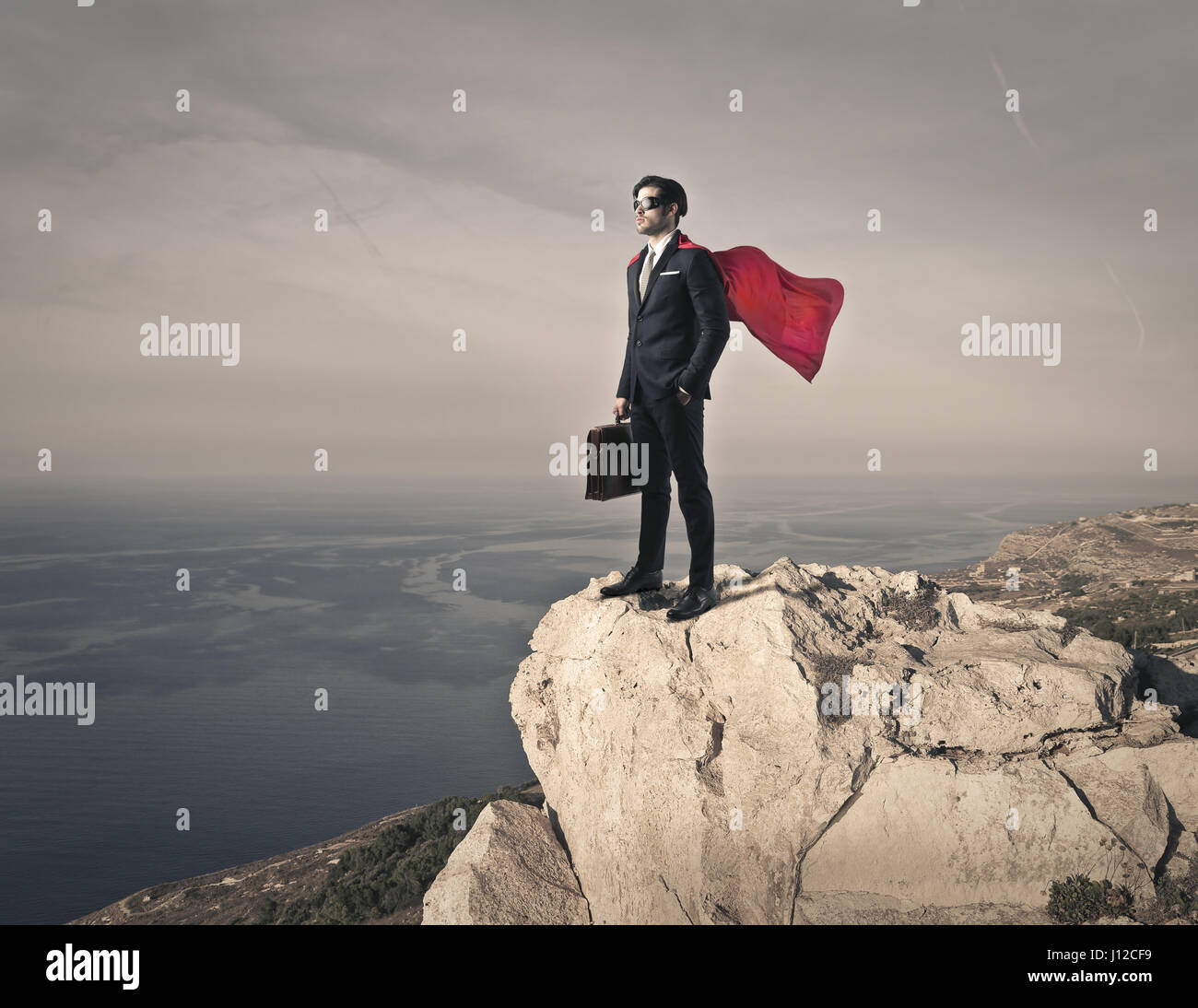 Man with cape standing on cliff Stock Photo