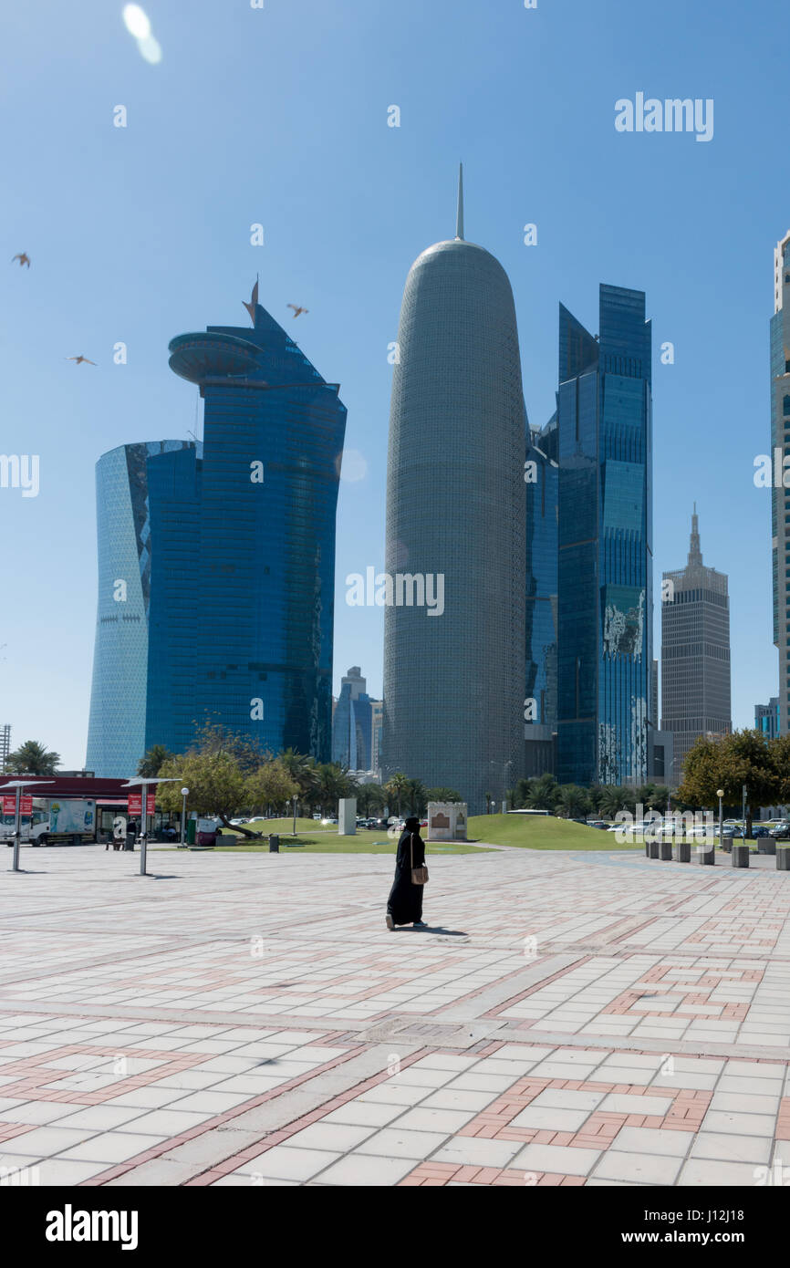 Doha Cityscape, Qatar, Middle East - one woman walking away from camera wearing a Shayla on her head and a black dress called an abayha. Stock Photo