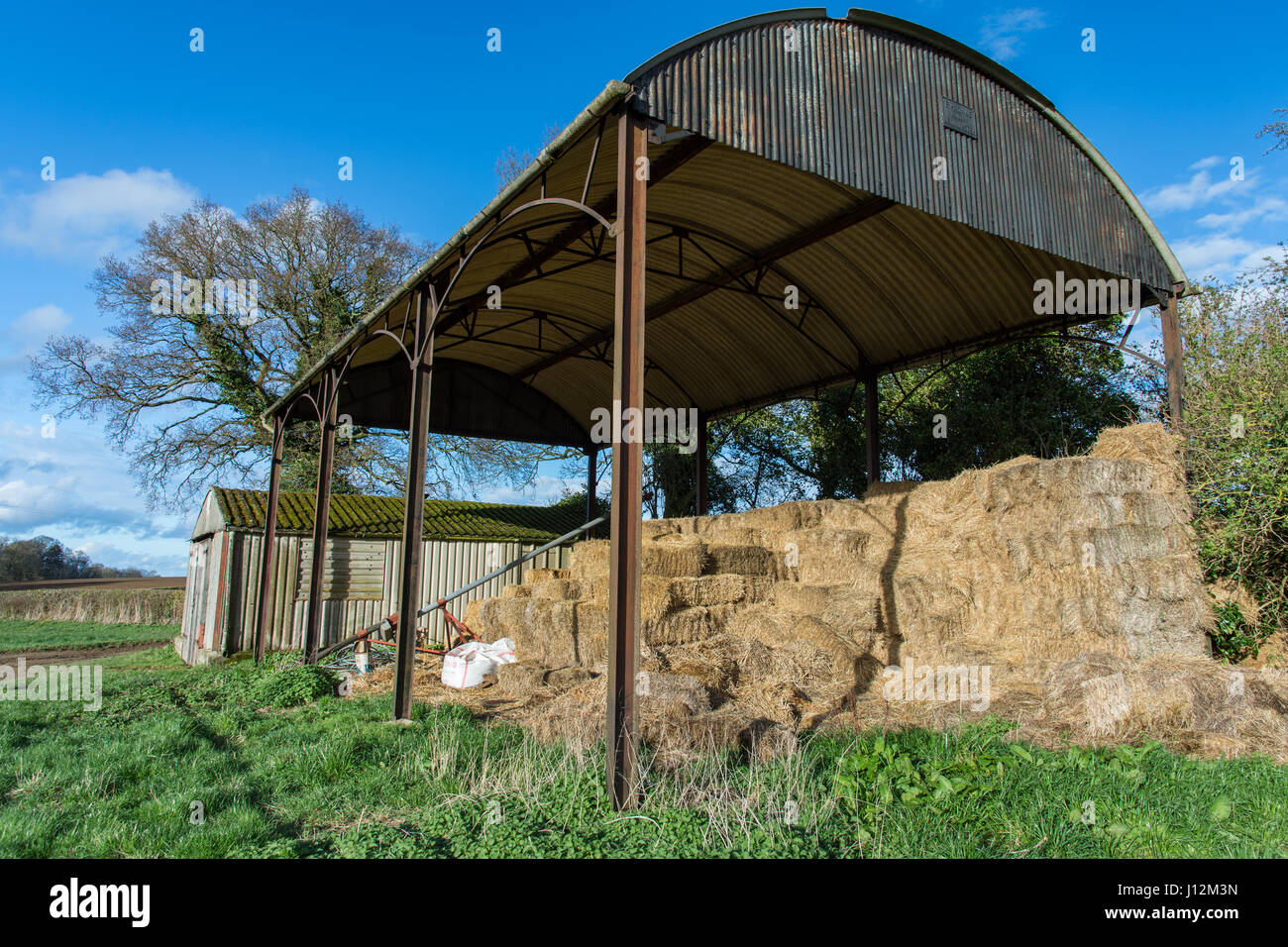 Classic open Cotswold barn with old hay bales against a blue spring sky Stock Photo