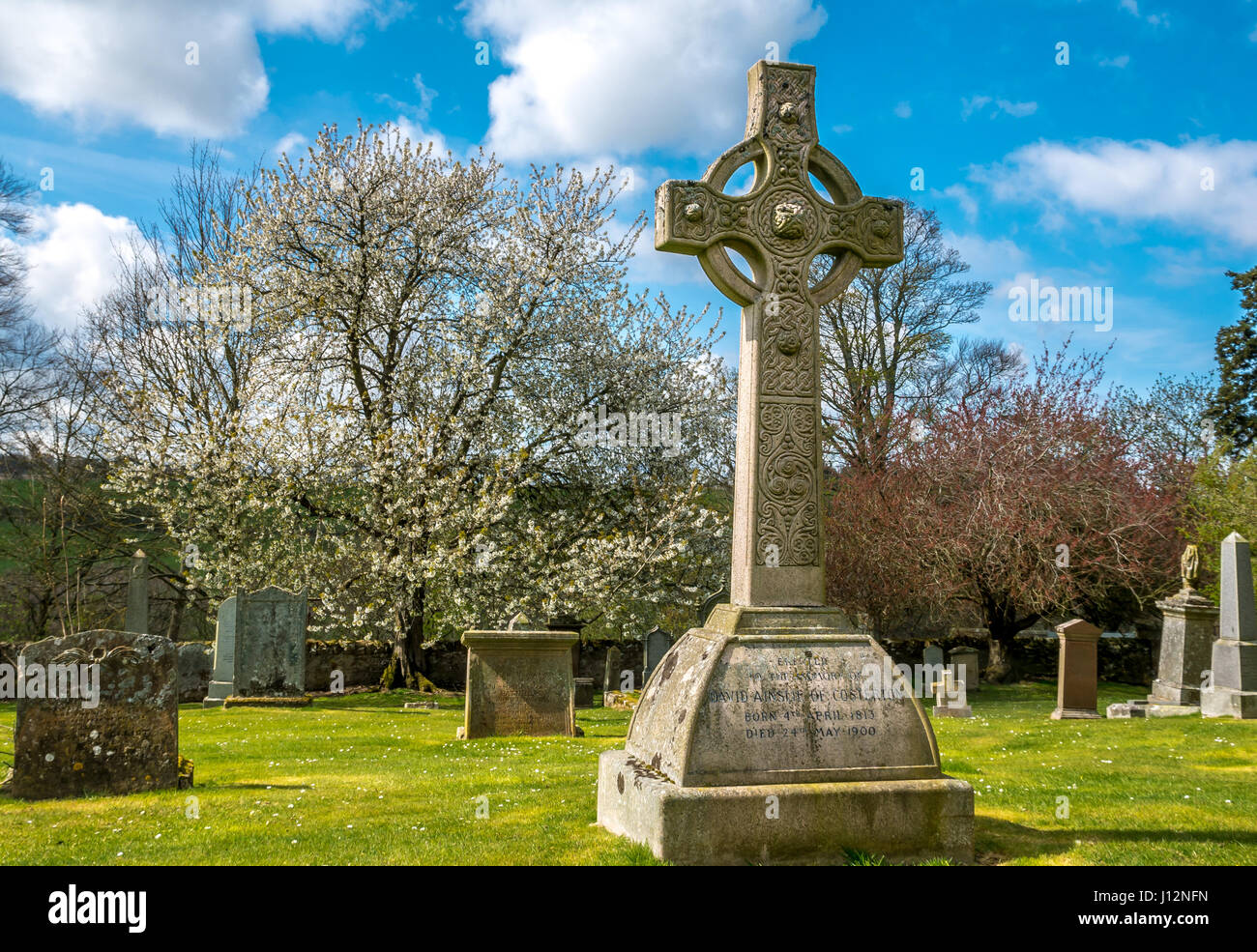 Celtic cross on grave and headstones in old churchyard with blue sky on