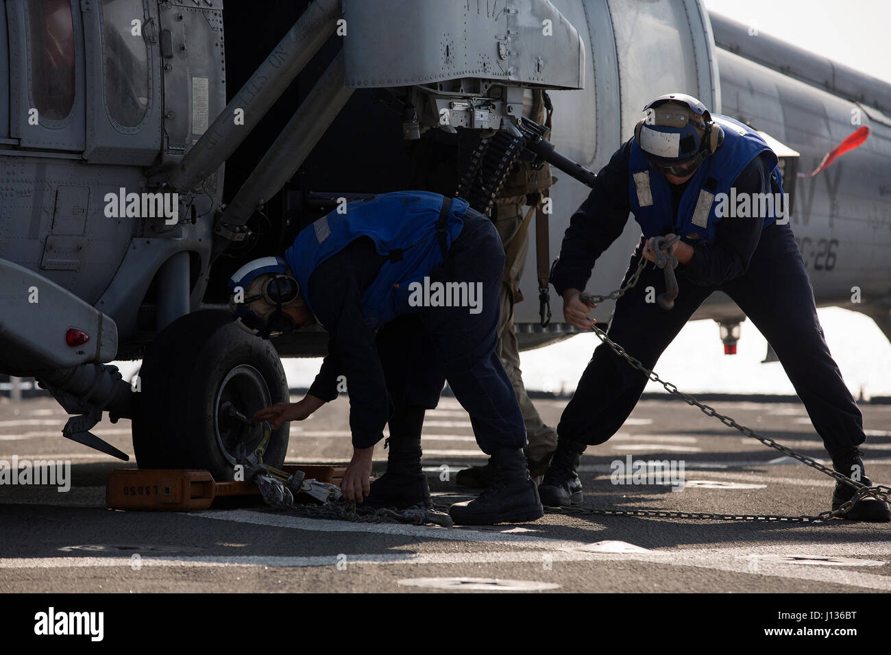 GULF OF ADEN (April 4, 2017) — U.S. Navy Seaman Jay Lao, left, and Petty Officer 3rd Class Derek Valenti, chain down an MH-60S Sea Hawk assigned to the Desert Hawks of Helicopter Sea Combat Squadron (HSC) 26, after it lands on the flight deck of the amphibious dock landing ship USS Carter Hall (LSD 50) during flight operations April 4. Carter Hall, part of the Bataan Amphibious Ready Group, is deployed to the U.S. 5th Fleet area of operations in support of maritime security operations designed to reassure allies and partners and preserve the freedom of navigation and the free flow of commerce  Stock Photo