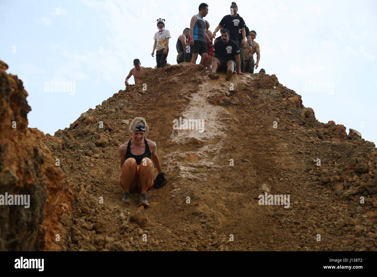 Military community personnel and Okinawa residents slide down a muddy hill April 9 during the annual World Famous Mud Run aboard Camp Hansen, Okinawa, Japan. Attendees ran one, three, five and 10-kilometer courses through mud and hills. The 10-kilometer course has been re-mapped and the second mud pit was enlarged since the first mud run. Participants received various prizes such as t-shirts, towels and medals. (U.S. Marine Corps photo by Sgt. Douglas D. Simons) Stock Photo