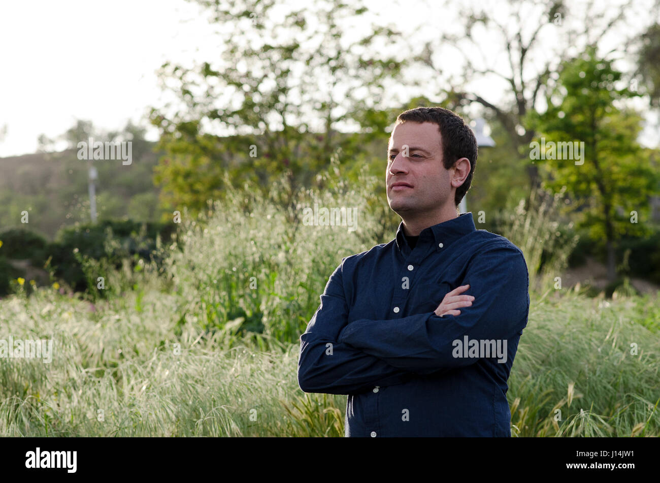 Man looking forward to the future in a grassy field with arms crossed. Stock Photo