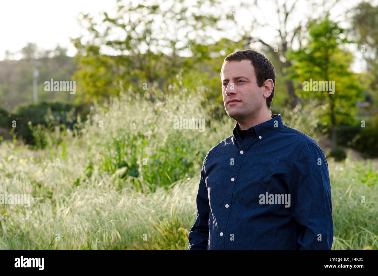 Man looking forward to the future in a grassy field with arms crossed. Stock Photo