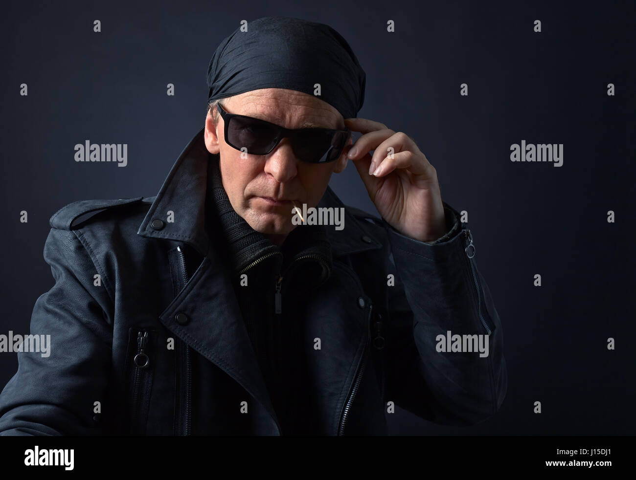 Portrait of a middle-aged man in a black leather jacket , sunglasses and black bandana .Rocker with sunglasses on black background. Stock Photo