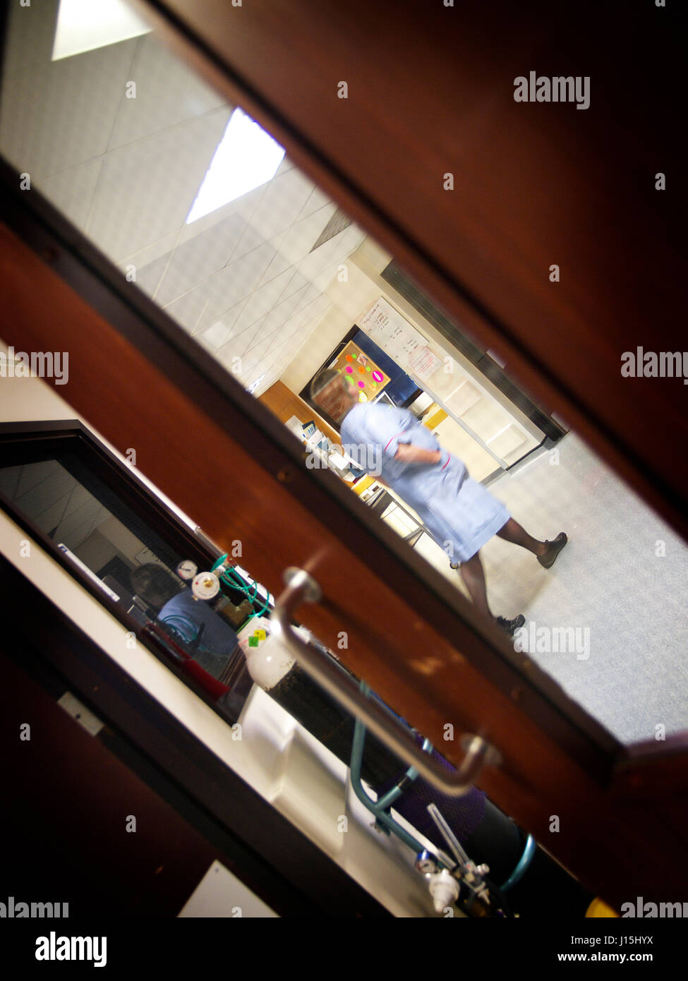 secret footage of NHS medical UK hospital View through window through to ward reception with medical staff walking in background Stock Photo