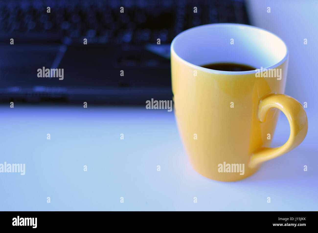 Yellow coffee mug with copy space. Laptop on background. Stock Photo