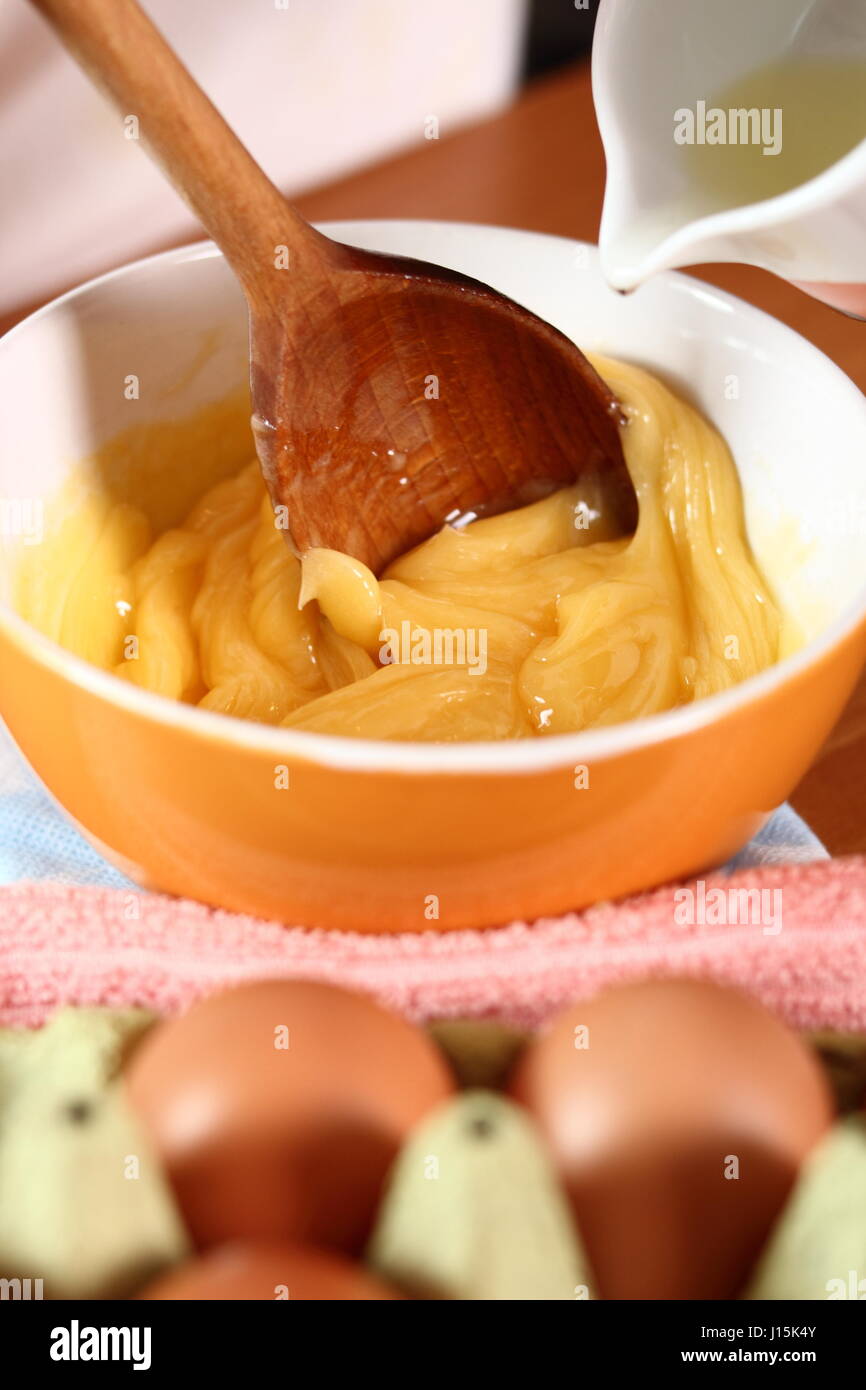 Pouring oil to an egg yolk. Making mayonnaise with a wooden spoon Stock