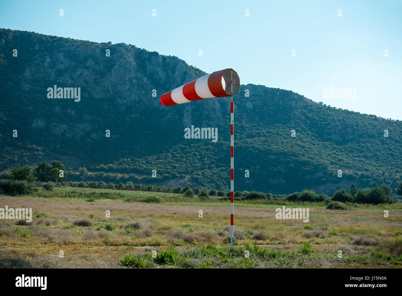 Horizontally flying windsock (wind vane) due to high wind. Blue sky and high mountains in the background. Stock Photo