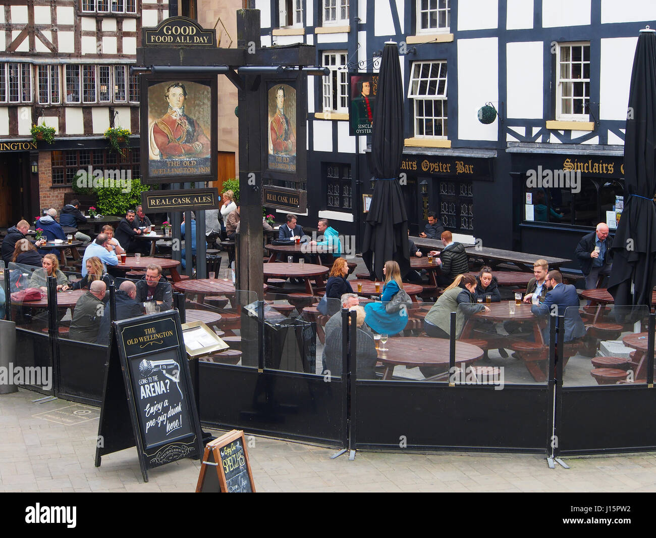 People relaxing with a drink and food outside the Sinclairs Oyster Bar and the Old Welllington Inn, in the centre center of Manchester, England, UK. Stock Photo