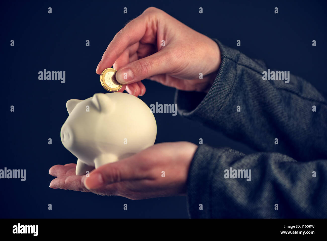 Depositing one euro coin into piggy coin bank for saving, close up of ...