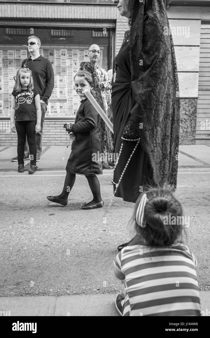 Linares, SPAIN - April 12: A girl dressed in typical suit of Spanish mantilla smiles to another girl sitting on the street facing the procession atten Stock Photo