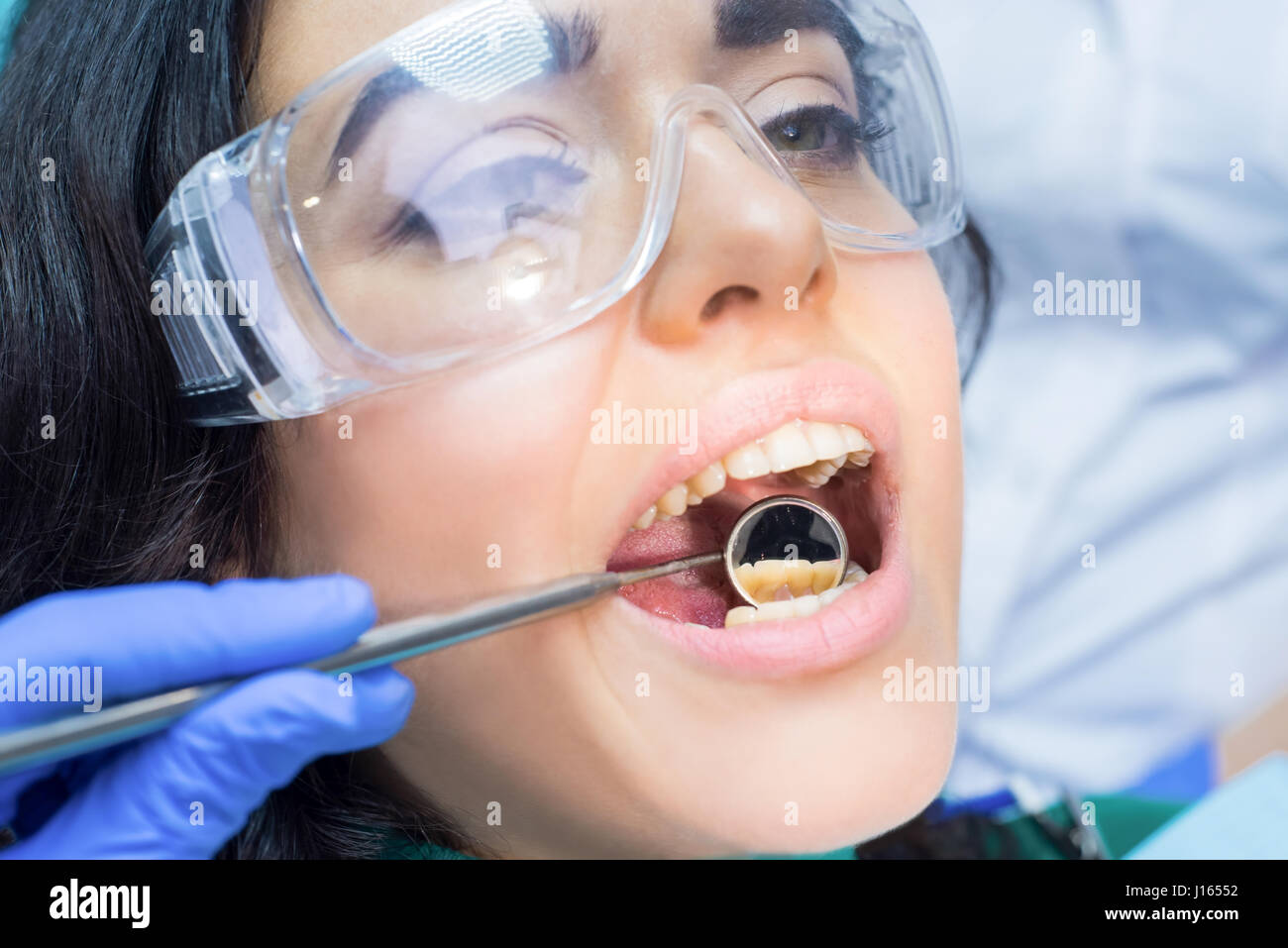 Stomatologist is using concave mirror. Female patient in safety glasses