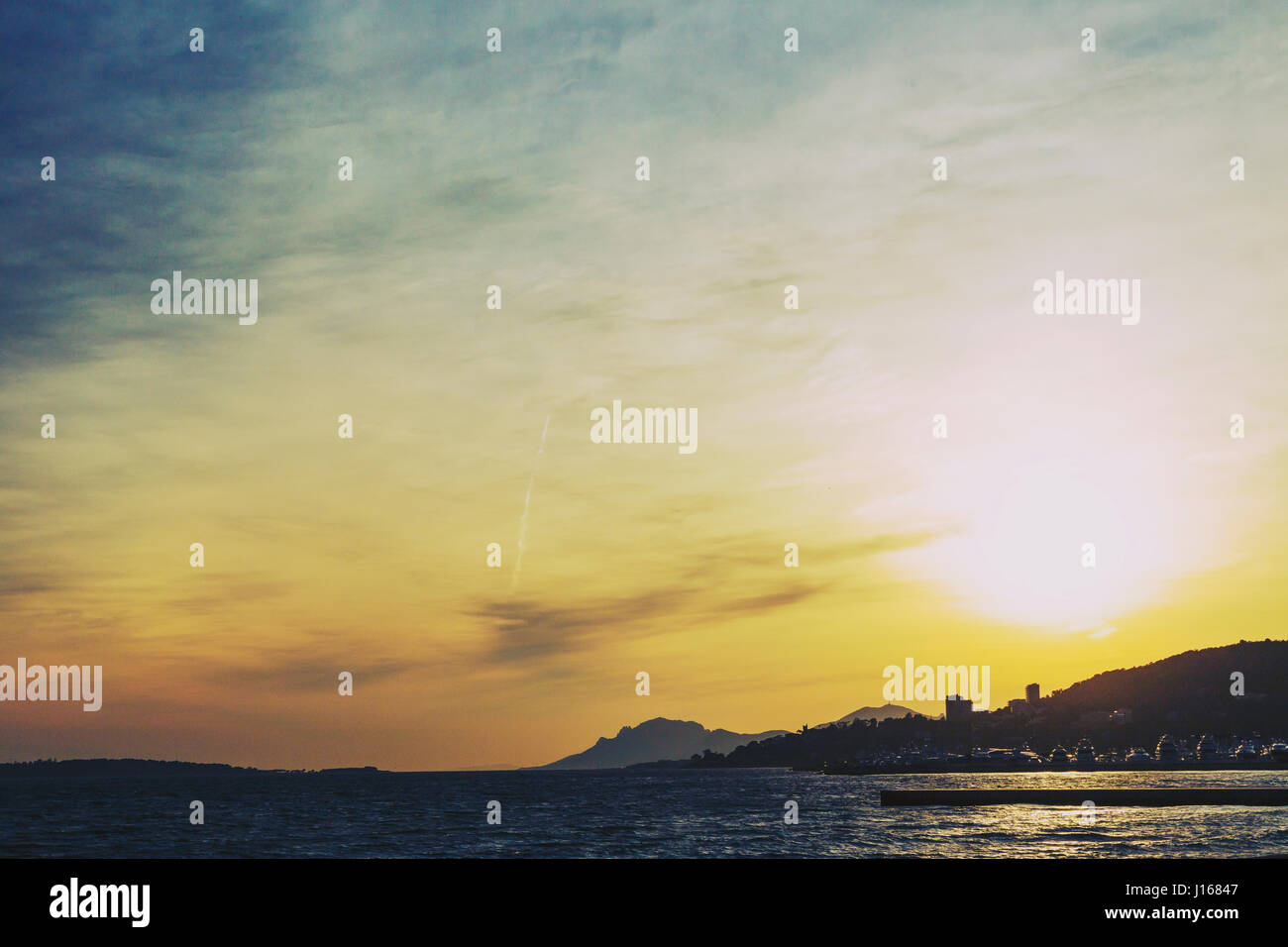 CANNES, FRANCE - 30 January, 2016: Mediterranean sea view from Golfe Juan at dusk with sun flare, with the Lerins Islands, the harbour and Cannes's co Stock Photo