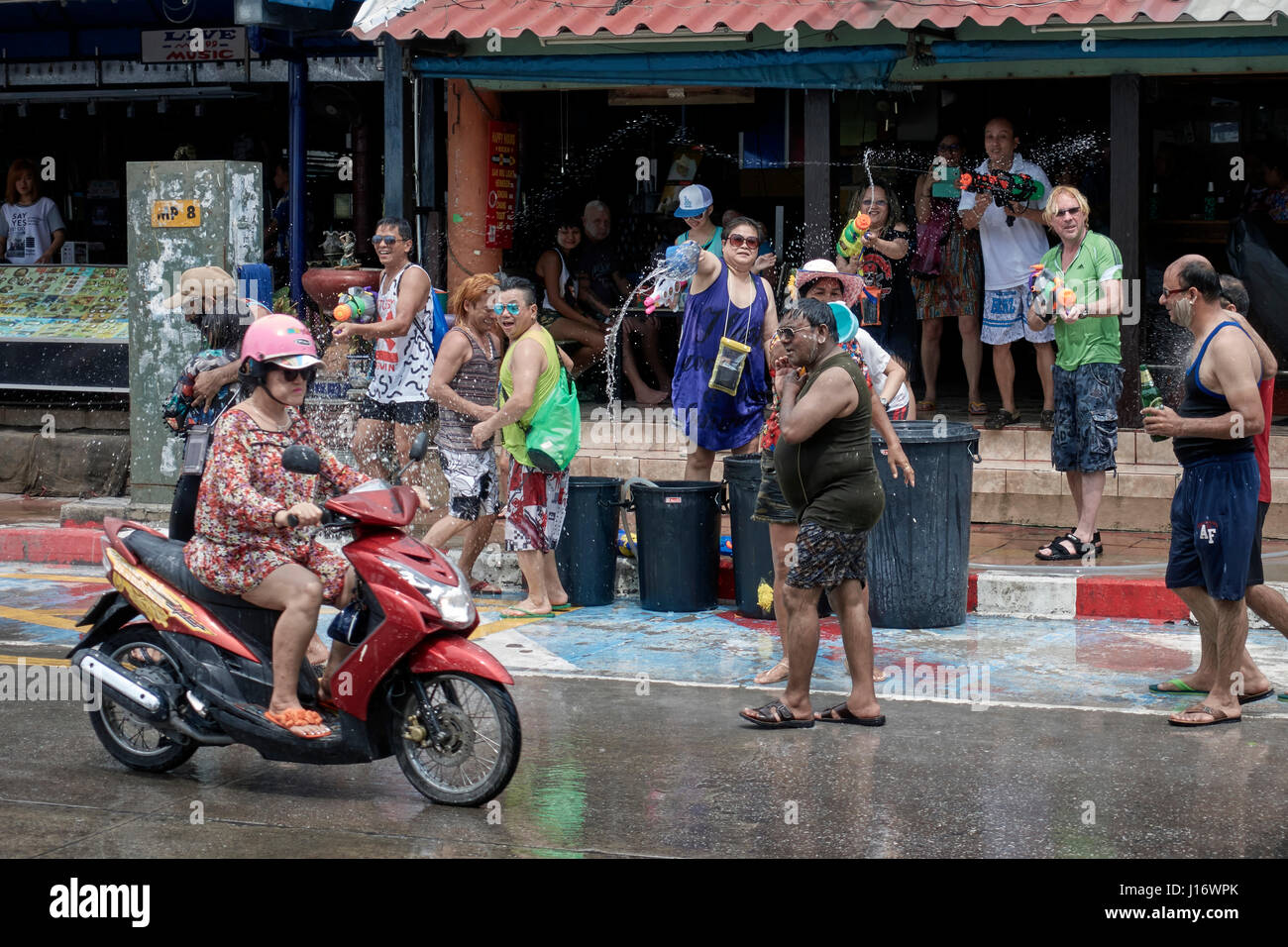 Songkran Thailand. Woman riding a motorcycle during the Thailand Songkran water festival. With people throwing water at her. Southeast Asia Stock Photo