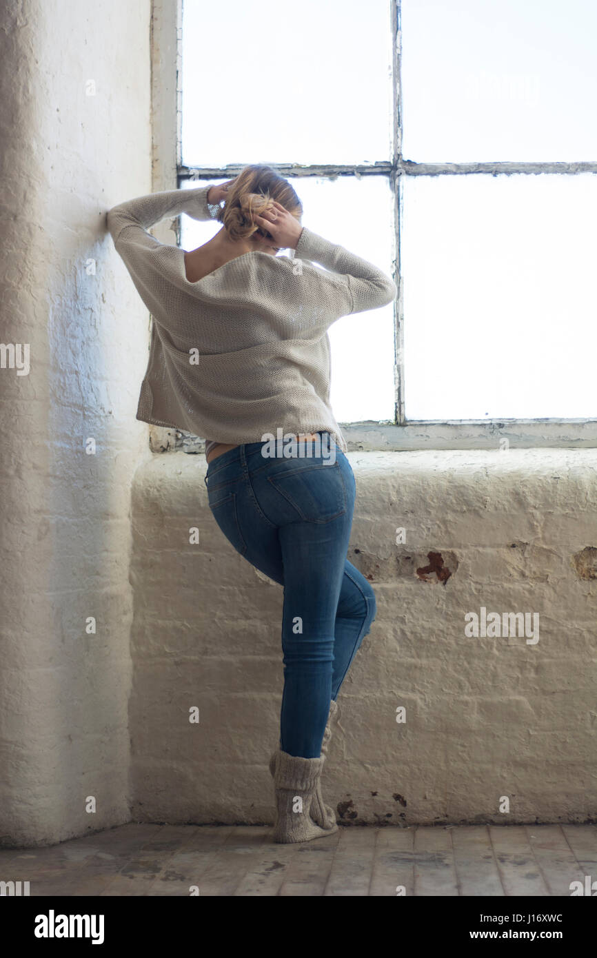 Rear view of a young blond woman standing by the window Stock Photo - Alamy