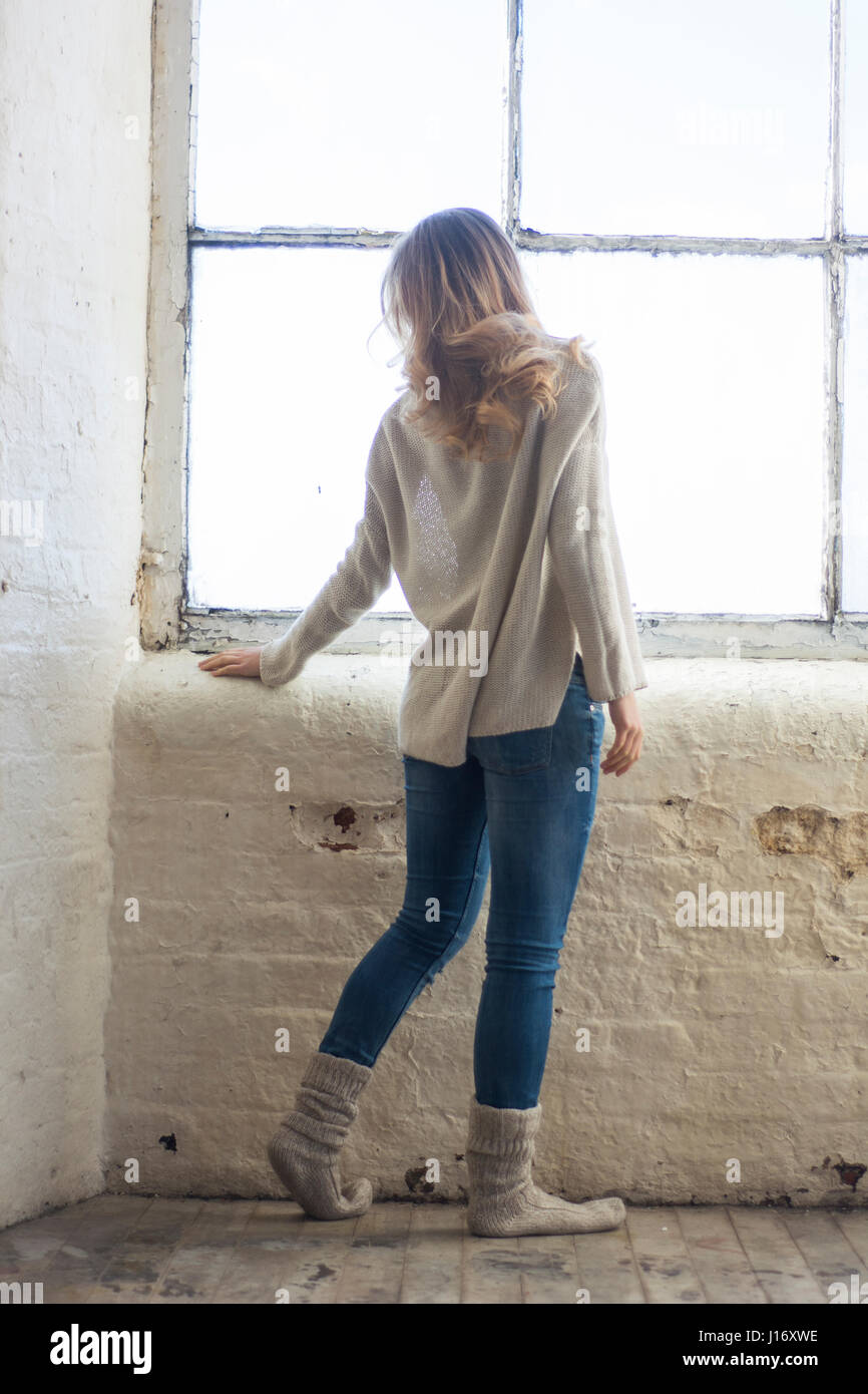 Rear view of a young blond woman standing by the window Stock Photo