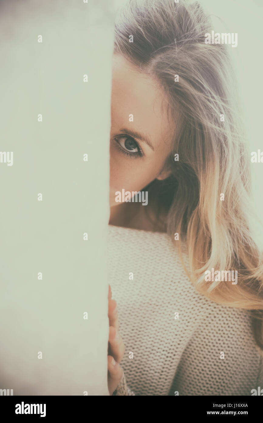 Young blond woman hiding behind the wall Stock Photo