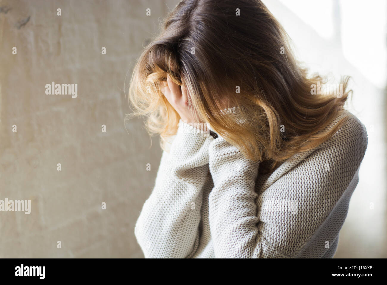 Young blond woman crying hiding face in hands Stock Photo