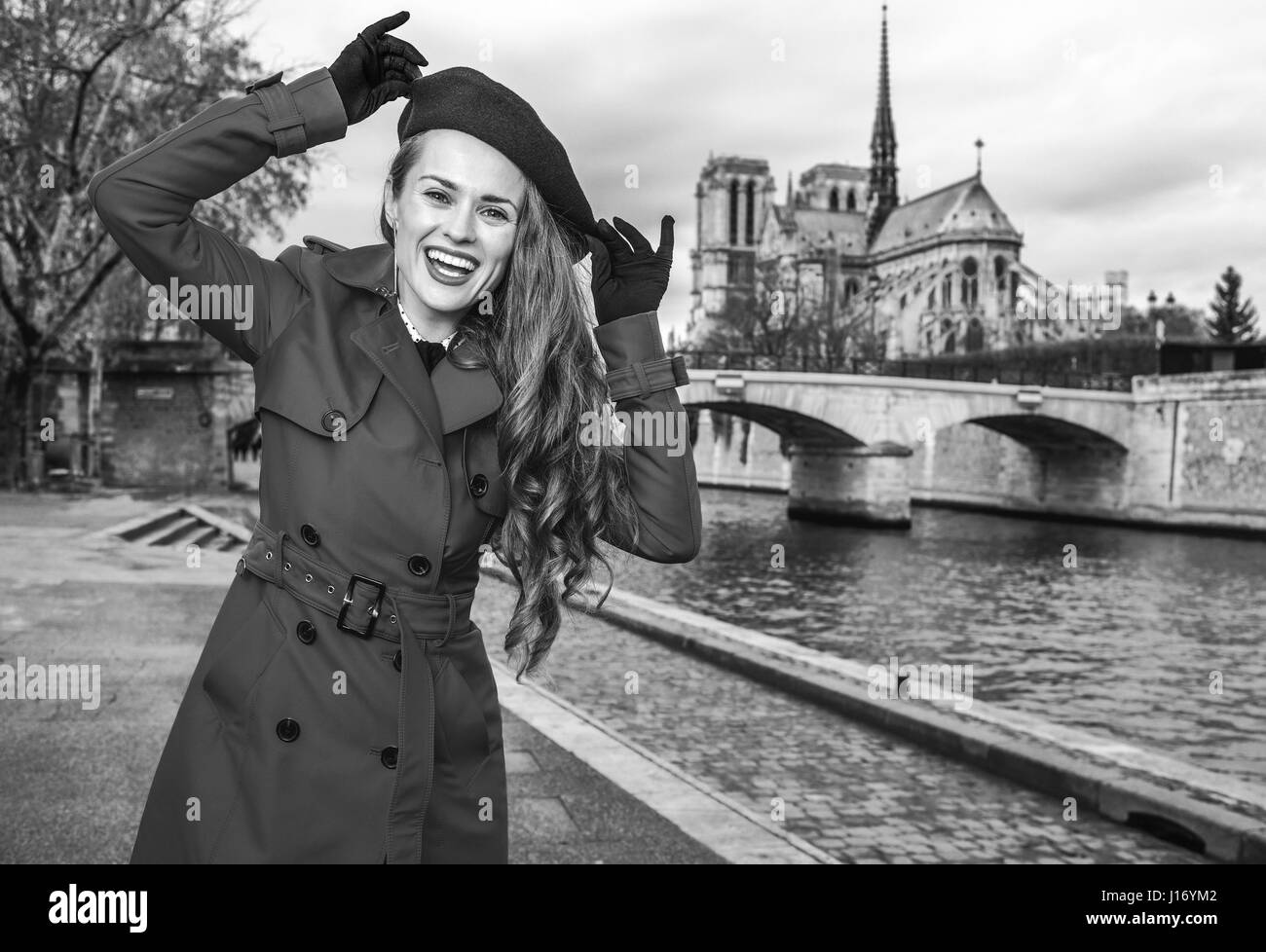 Bright in Paris. Portrait of smiling modern woman in red trench coat on embankment in Paris, France having fun time Stock Photo