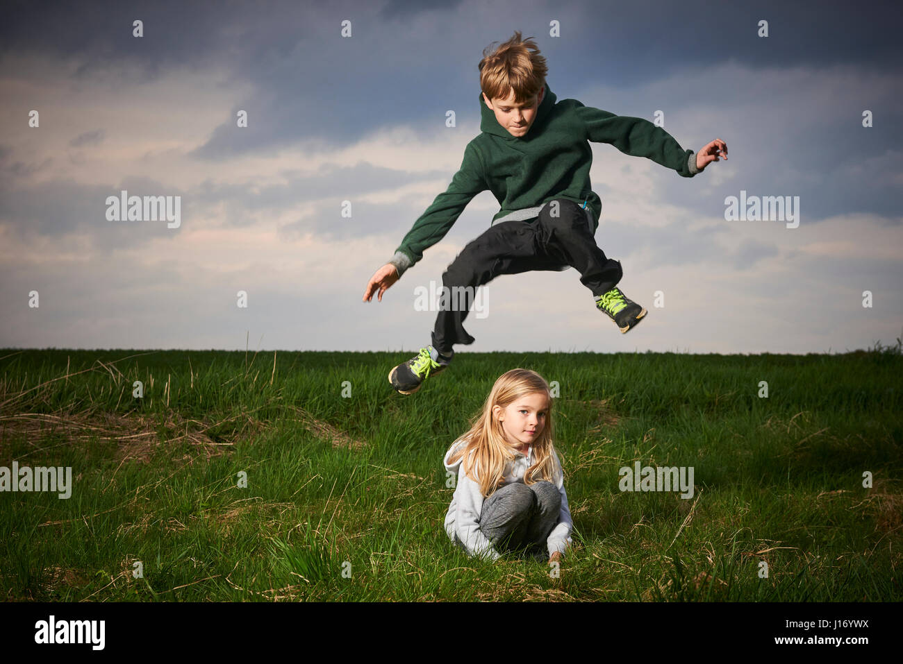 Brother Jumping Over Sister In Meadow Cloudy Sky Background Children Summer Outdoor Activities Jumping High And Far Brother Jumping Over Sister In Meadow Cloudy Sky Background Children Summer Outdoor Activities Jumping High And Far