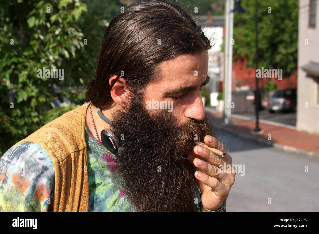 Man with long hair and beard, smoking on the street Stock Photo