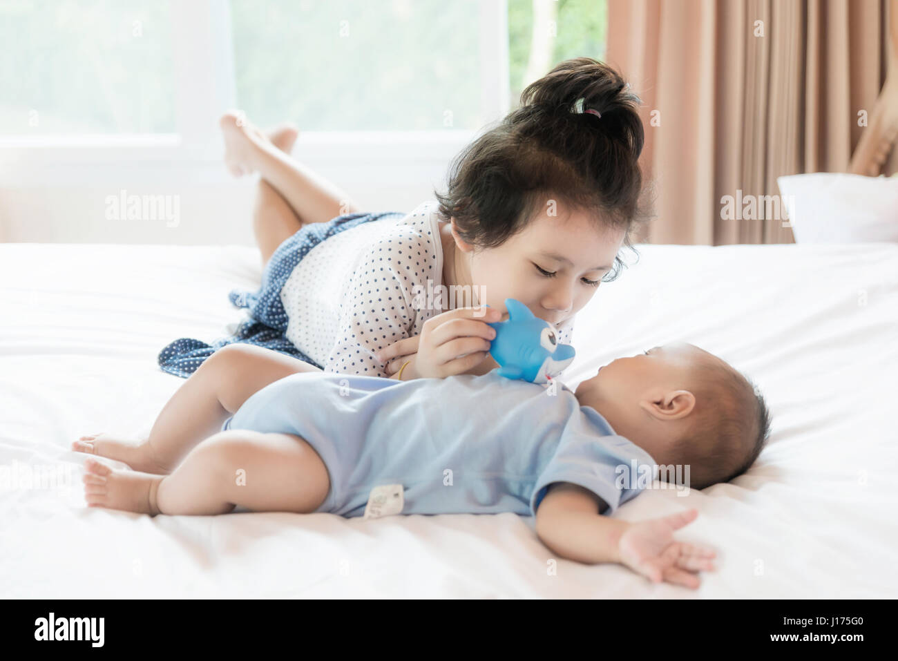 Asian baby brother and toddler sister playing fish doll in bedroom. Happy family. Stock Photo