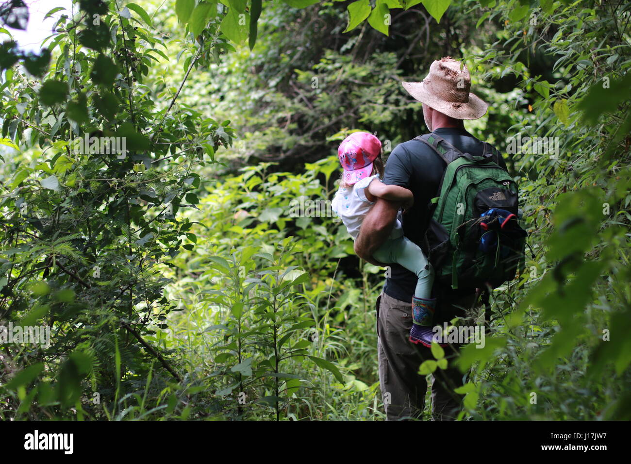 father and daughter hiking on lush green mountain trail Stock Photo