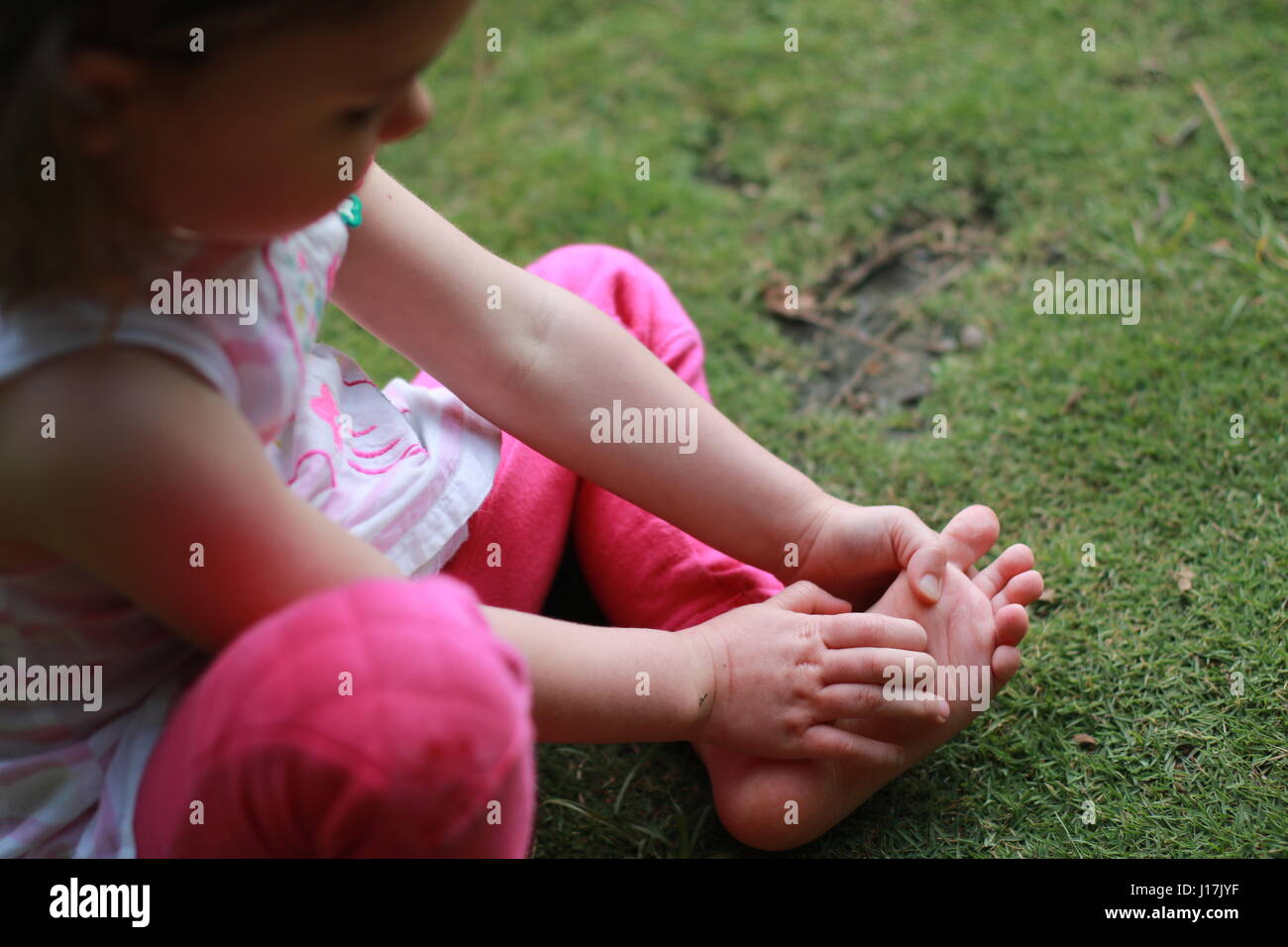 young girl inspecting the sole of her foot sitting barefoot on grass Stock Photo