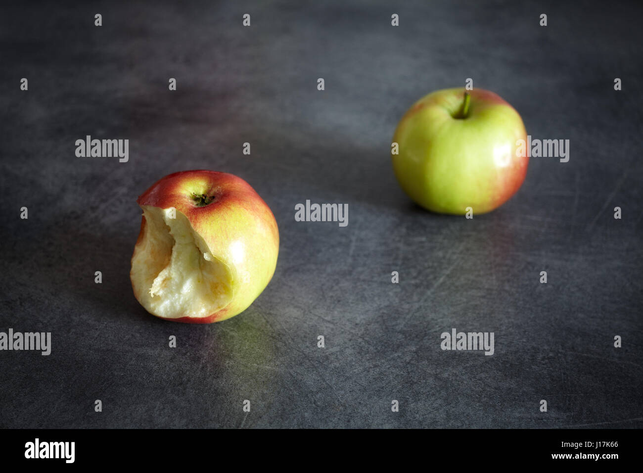 Two ripe apples, one bitten and one whole on a dark background, selective focus, space for text. Stock Photo