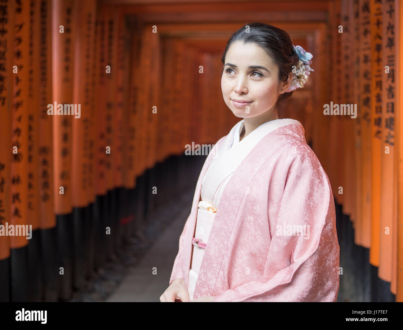 Young Japanese woman in kimono walking through the tunnel of torri ...