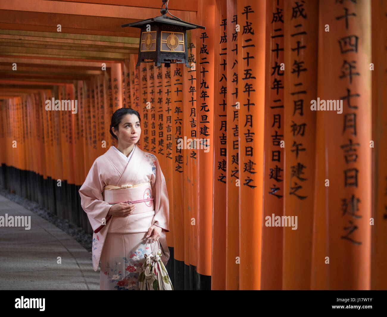 Young Japanese woman in kimono walking through the tunnel of torri ...