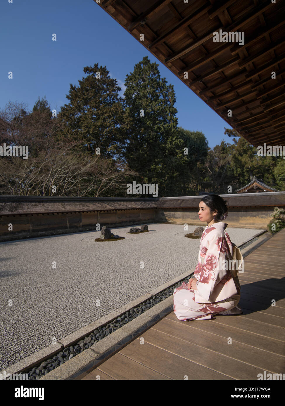 Young Japanese woman in kimono kneels beside The rock garden at Ryoan-ji, Kyoto. One of the finest examples of a hire-niwa stone garden. Zen meditatio Stock Photo