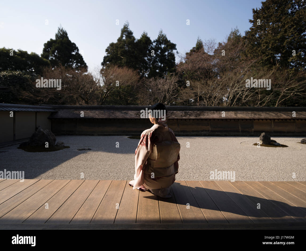 Young Japanese woman in kimono kneels beside The rock garden at Ryoan-ji, Kyoto. One of the finest examples of a hire-niwa stone garden. Zen meditatio Stock Photo