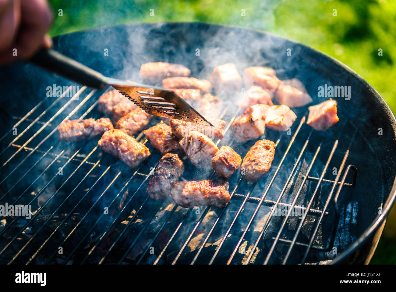 Grilling delicious variety of meat on barbecue charcoal grill. Grilling food on a weber type small cheap BBQ grill at home. Family backyard barbecue - Stock Photo