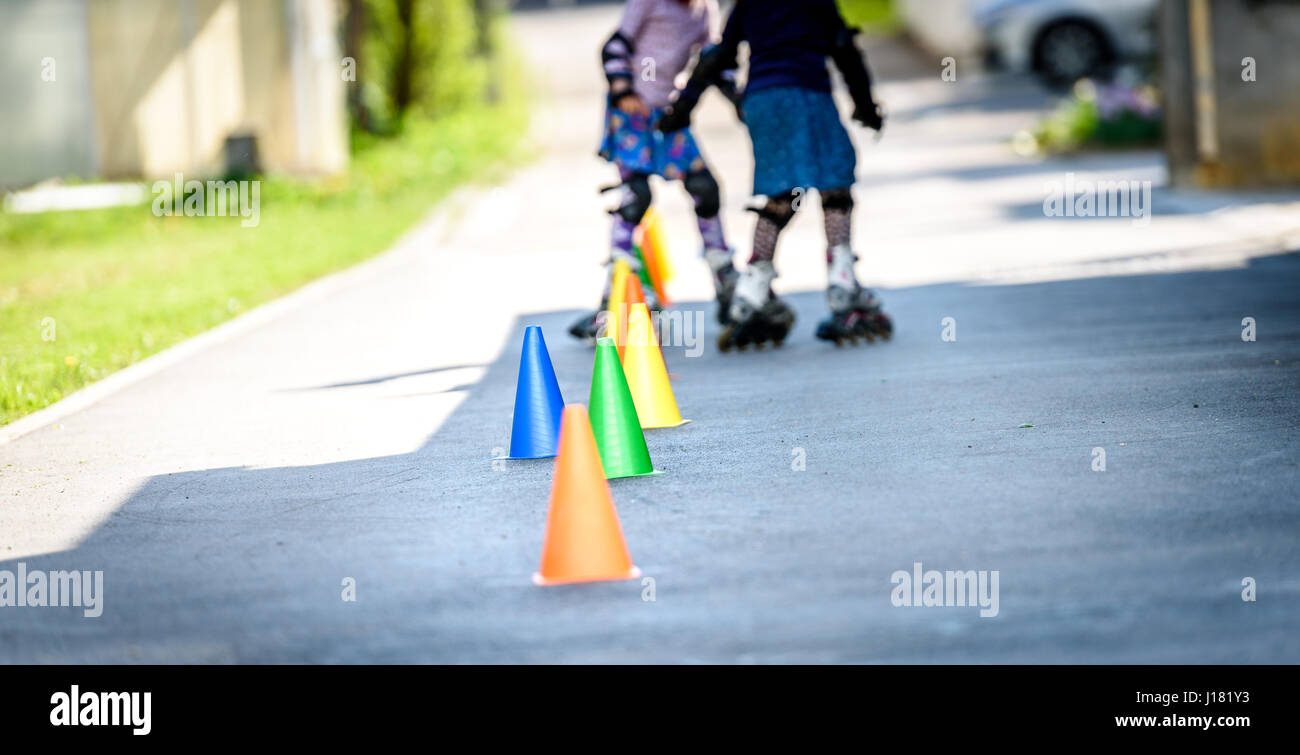 Children learning to roller skate on the road with cones. Twin girls are practising safe roller