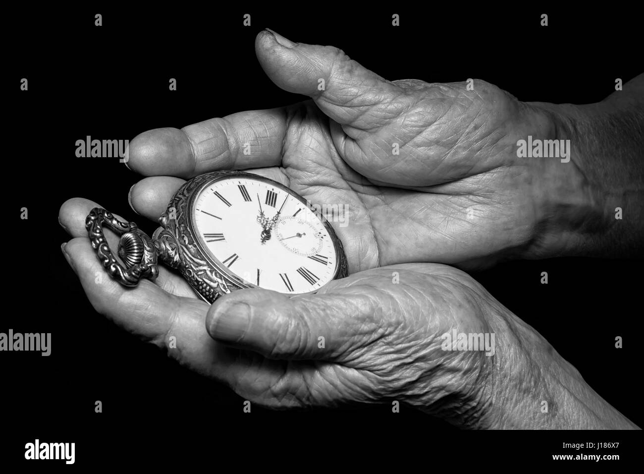 Senior woman hands holding ancient clock. Aging problems, senior age and stream of time theme. Black and white photo on black background Stock Photo
