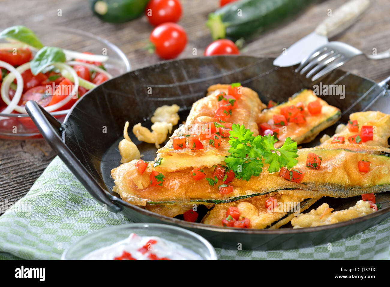Crispy coated zucchini slices, served in an iron pan with chili yogurt dip and tomato salad Stock Photo