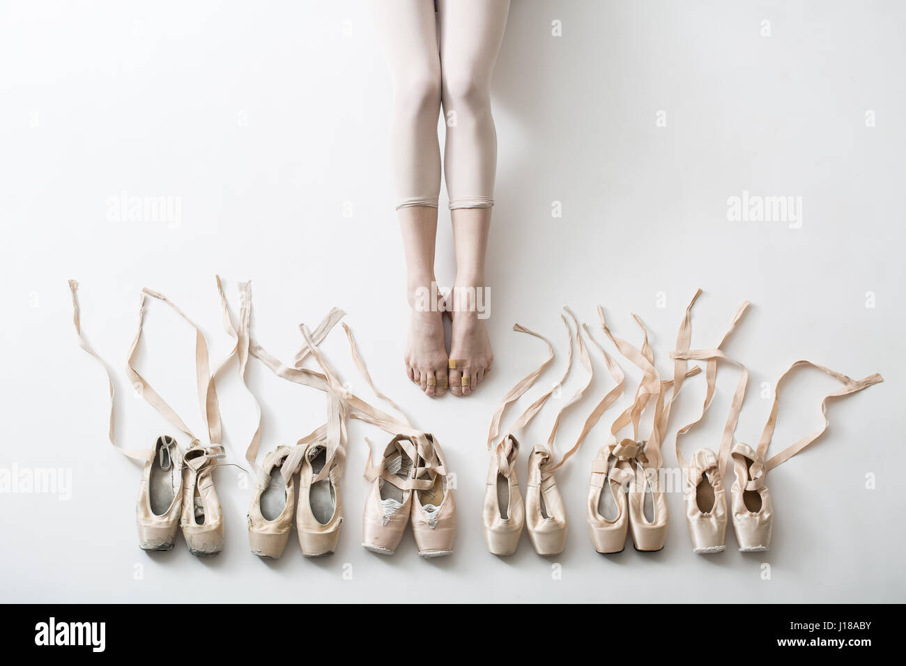 Many pairs of ballet shoes in pairs stand in a row. Legs of a young  ballerina with bare feet. The girl's fingers are all covered in wounds and  plaster Stock Photo -