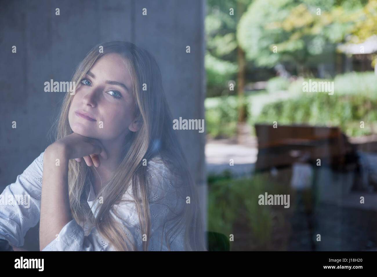 Young serious woman sitting in cafe photographed through window glass from outside with copy space Stock Photo