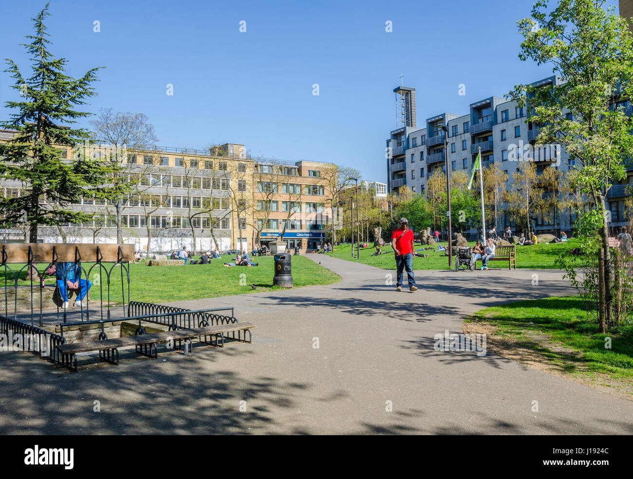 People relax in Altab Ali Park on Whitechapel Road in London on a warm, sunny spring day. Stock Photo