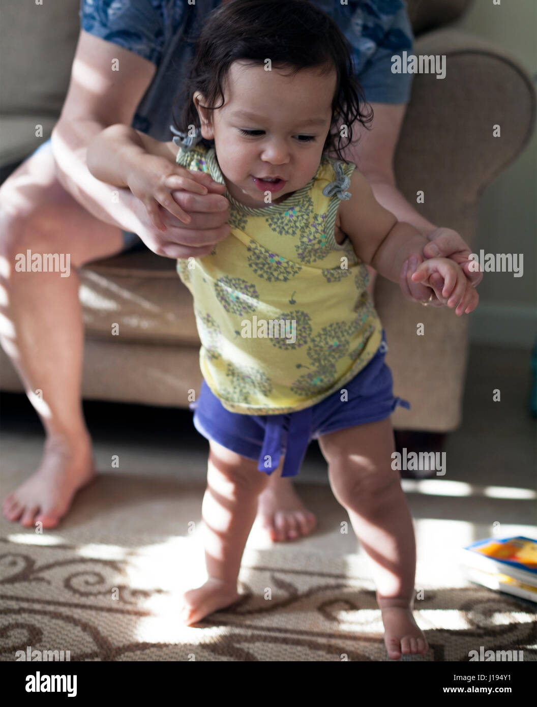 A young girl is learning to walk with the help of her grandmother. Stock Photo