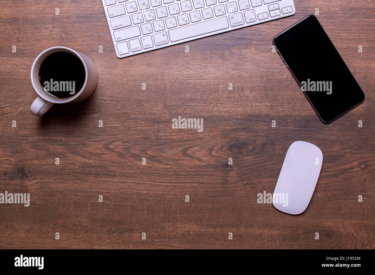 A keyboard, a mobile phone, a white cup of tea and a computer mouse on ...