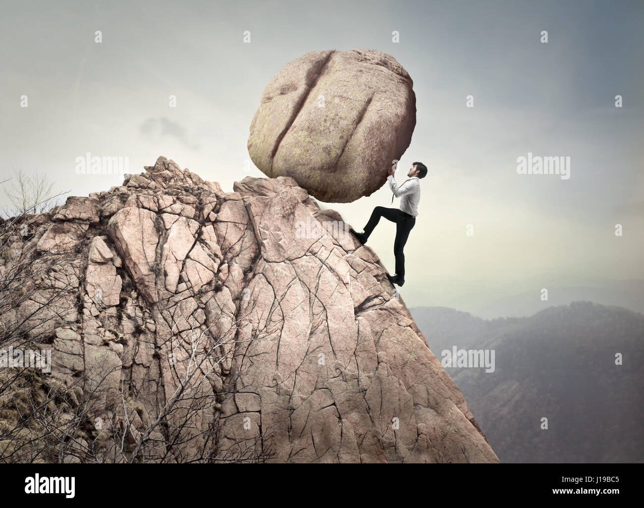 Businessman pushing rock on mountain Stock Photo