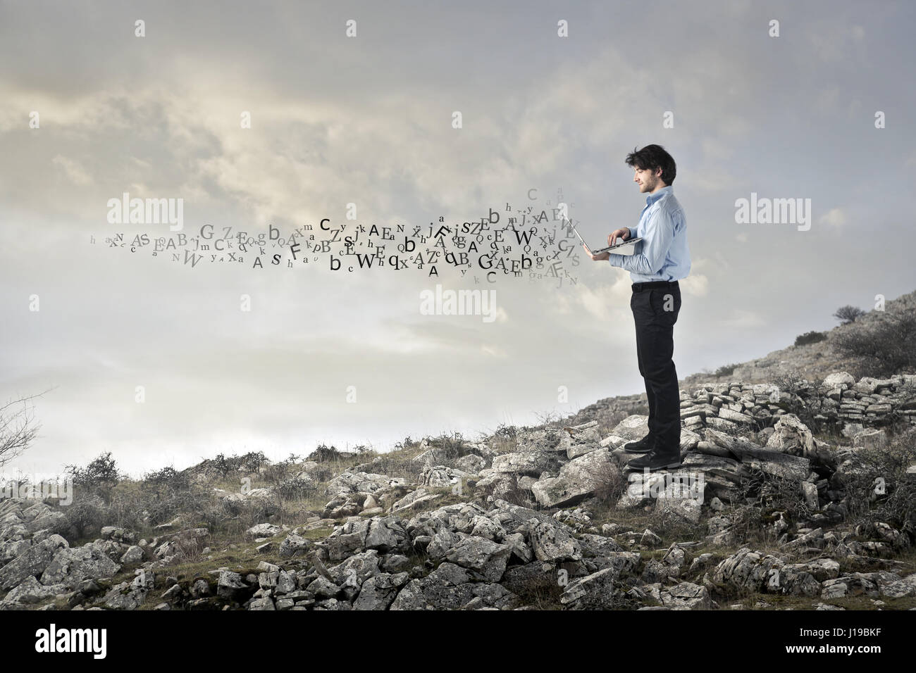 Businessman on mountain scattering letters Stock Photo