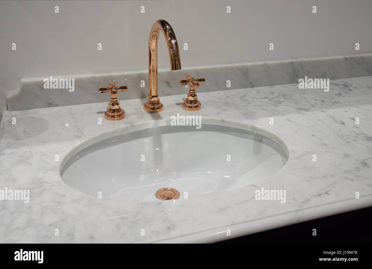 White inset ceramic washbasin in marble table and copper metal mixer Stock Photo