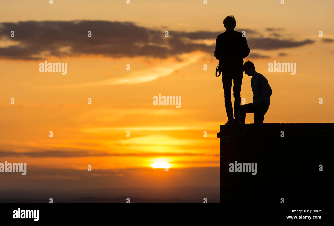 Silhouette of 2 friends standing on a wall in the evening watching the sun go down. Stock Photo