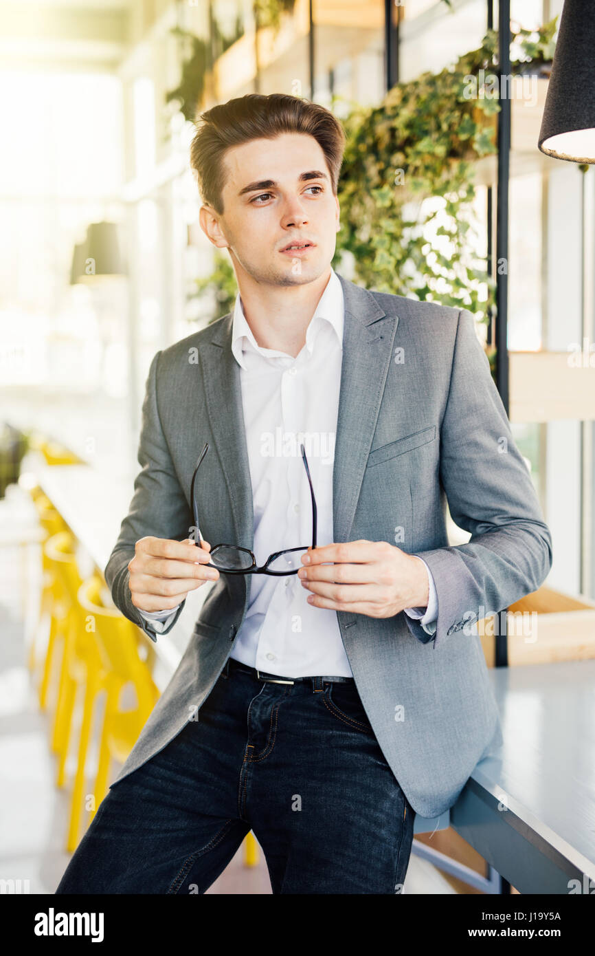 Young businessman with his arms folded and sitting on the edge of his wooden desk looking seriously at the camera Stock Photo