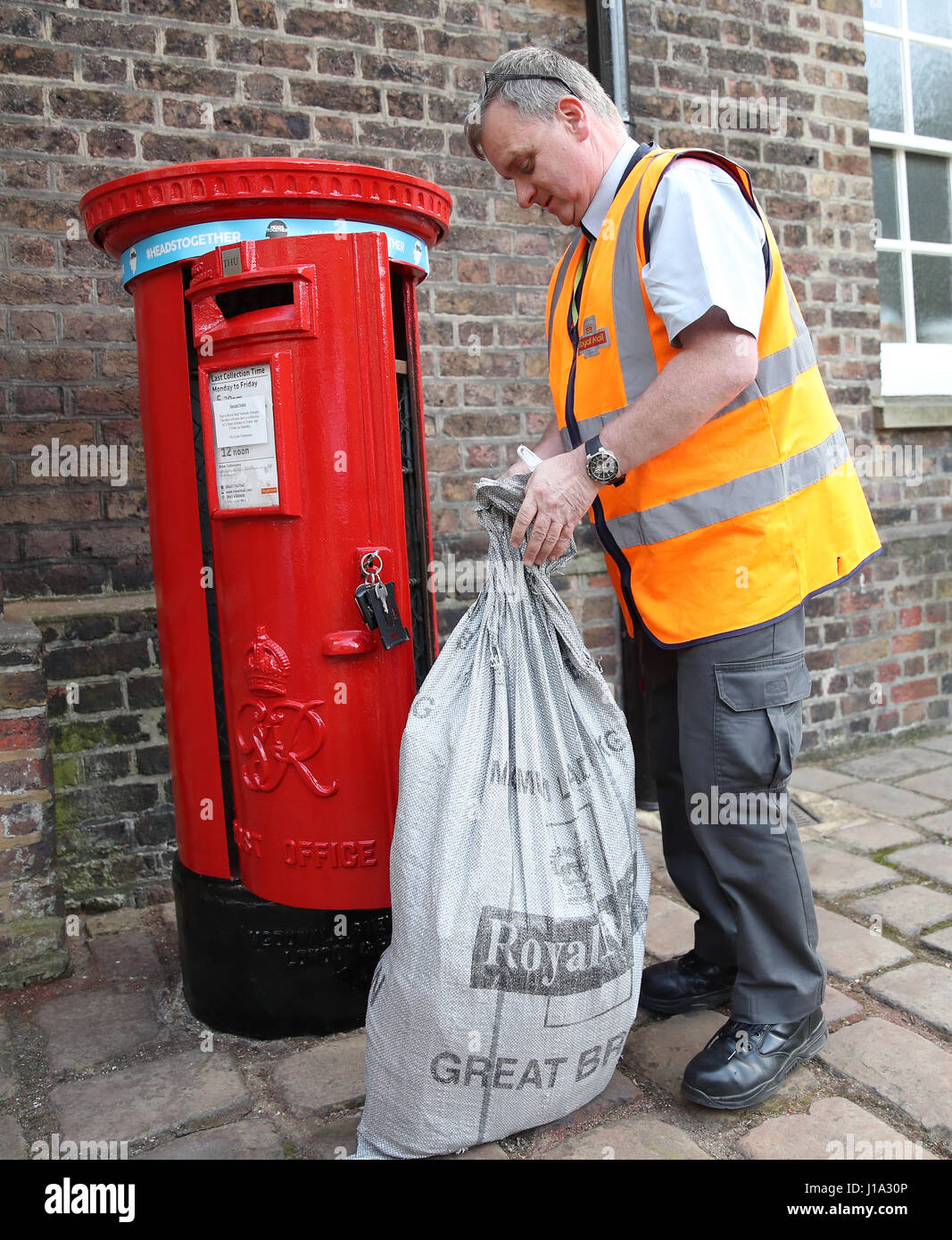 A postman empties the Kensington Palace postbox displaying a Heads