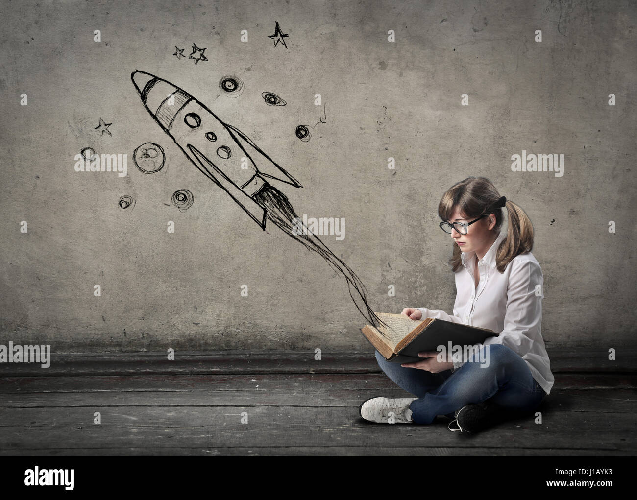 Girl reading book with imaginary rocket Stock Photo